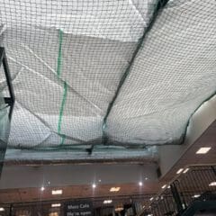 A ceiling covered with netting and white sheeting, likely for maintenance or construction. Below, a sign reads "Mezz Café We're open as usual," and stairs lead up to the café area.
